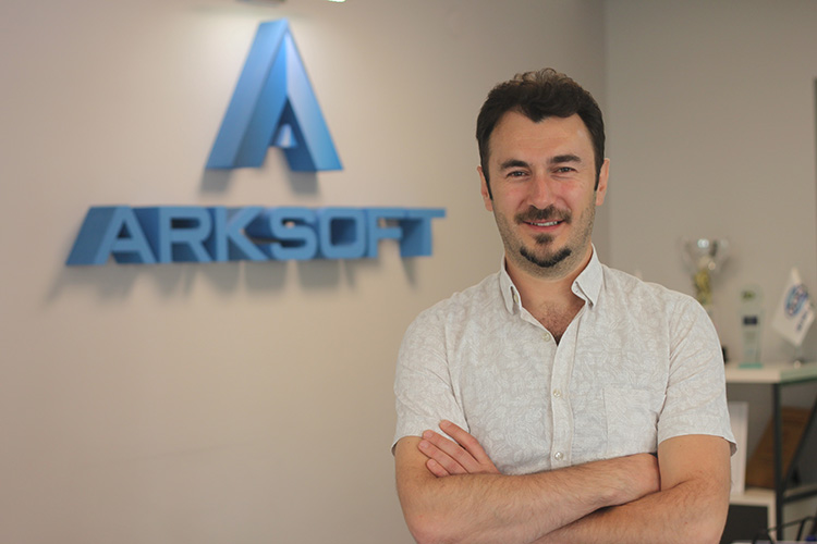 Boran Düzgün, COO of ARKSOFT, smiling with arms crossed in front of the company logo