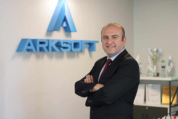 Tahir Emre Esirgen, CEO of ARKSOFT, standing with crossed arms in the office, with the company logo in the background
